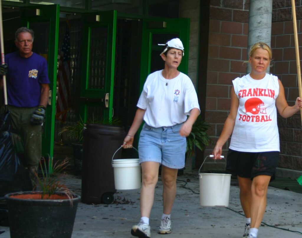 Two adults carrying buckets while doing hurricane repair.