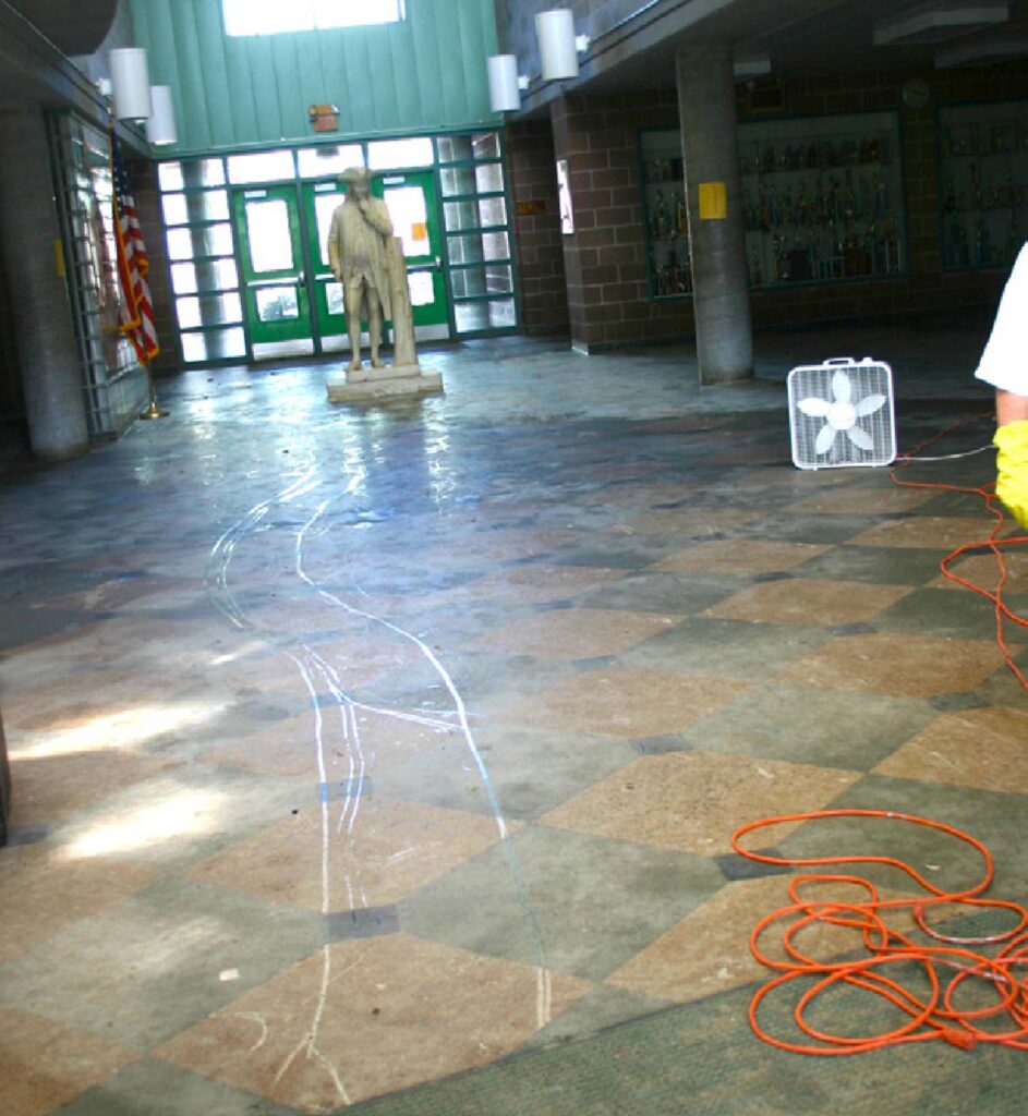 Box fan drying off a wet floor with a dirty state of Ben Franklin in the background.